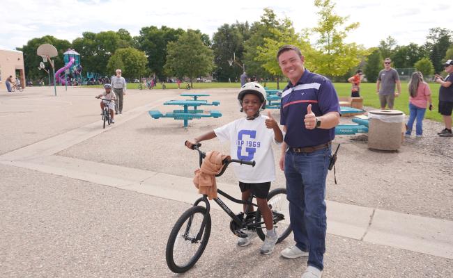 Principal Garcia posing with a second grader and his new bike